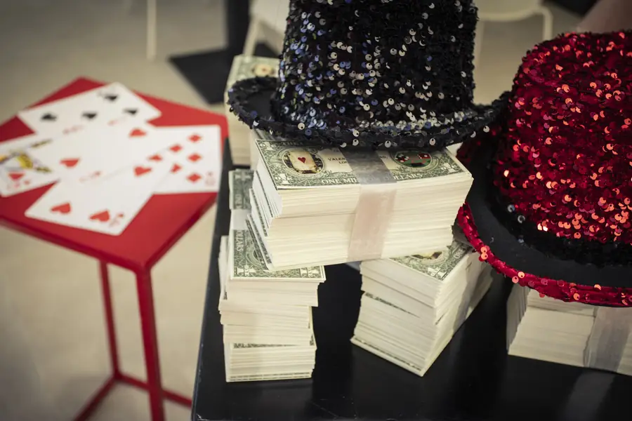 Sequin top hats, stacked prop million-dollar bills and playing cards on a red side table