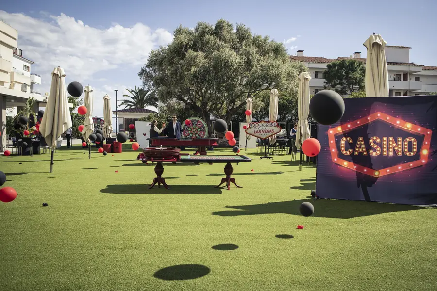 Casino gaming tables and a glowing Casino marquee on a lawn dotted with red and black balloons