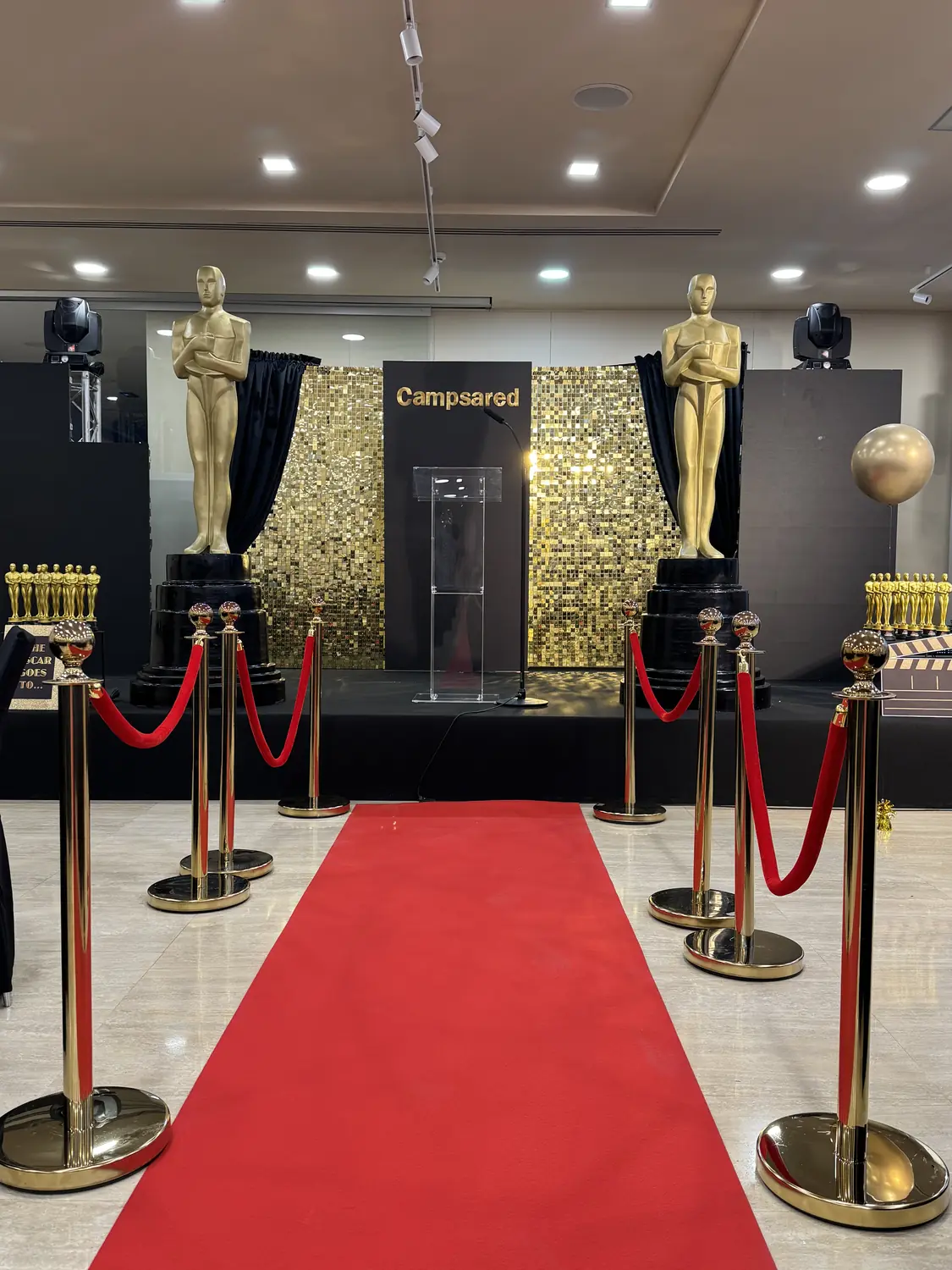 Red carpet flanked by giant gold award statues and a gold sequin backdrop at a corporate awards gala