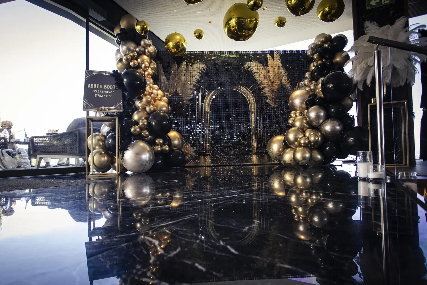 Black and gold balloon and gold-sphere installation reflected in a mirror-black marble floor