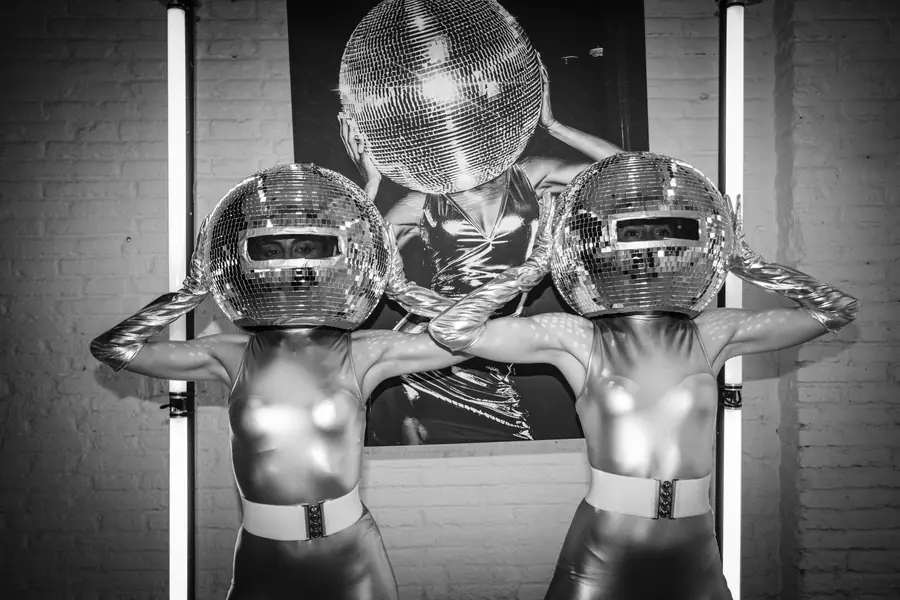 Silver performers dancing beneath an illuminated arch, in black and white