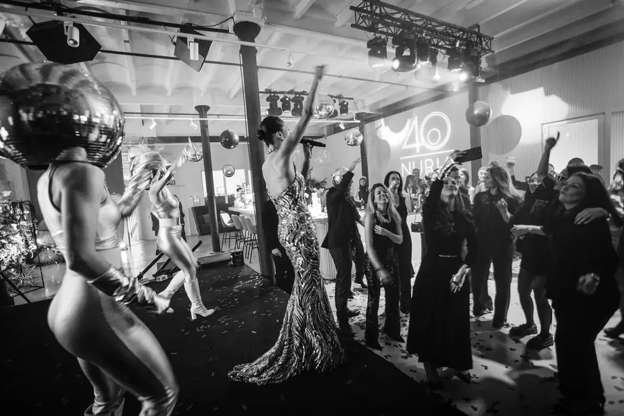 Sparklers held high over a crowded dance floor as a singer in sequins performs, in black and white