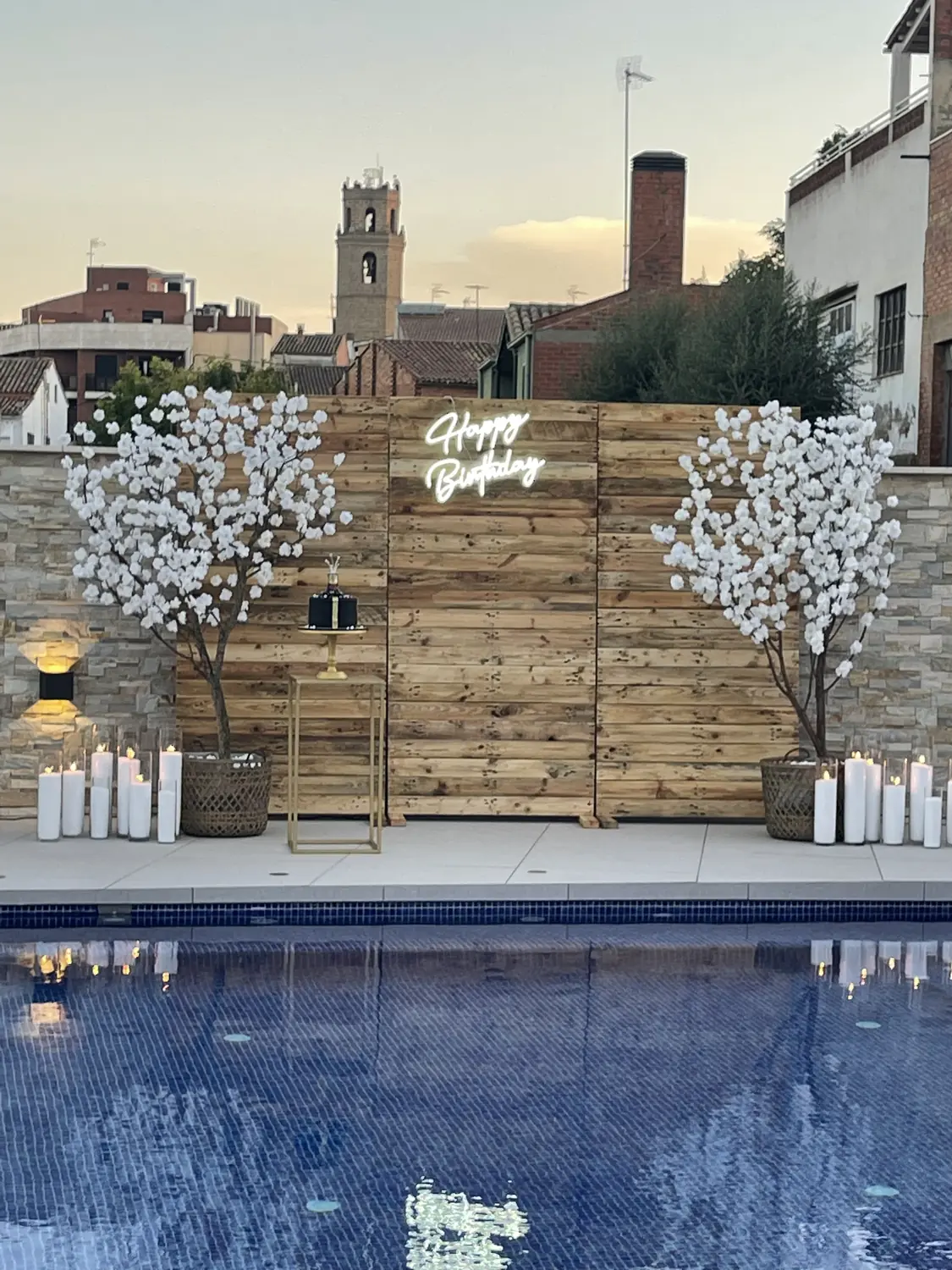 Private villa pool at dusk lined with white pillar candles beneath blossom trees