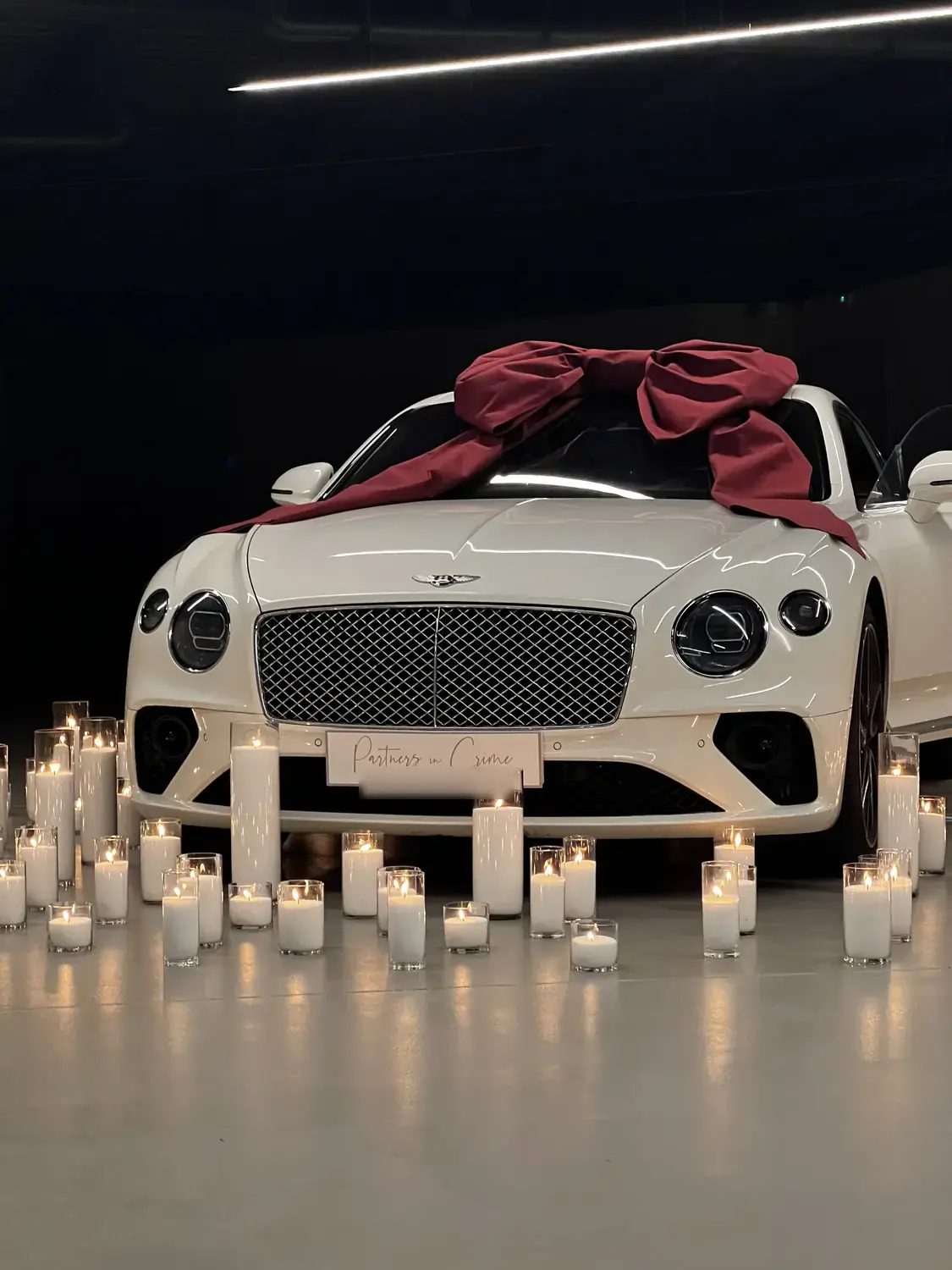 White Bentley tied with a red ribbon, surrounded by hundreds of candles in a darkened hall