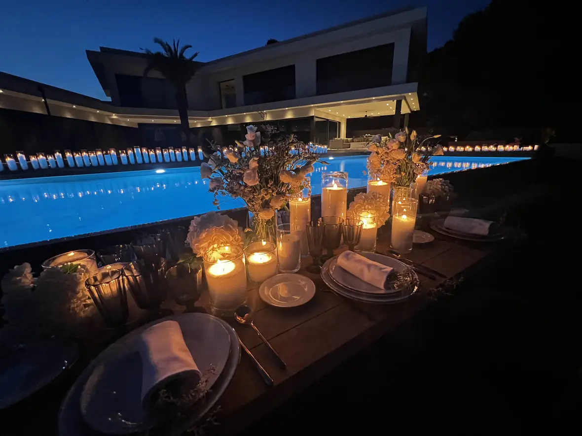 Elegant candlelit dinner table set beside the pool at dusk